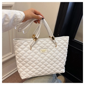 Detail of white quilted tote bag with gold hardware and removable shoulder strap