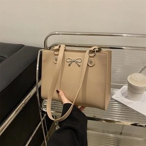Modern beige leather tote bag with silver bow accent shown in a stylish indoor setting