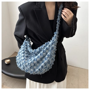 Detail shot of distressed blue and white checkered denim crossbody bag with frayed edges