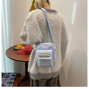 Detail of light blue canvas crossbody bag with adjustable strap and fashion patch