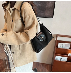 Side view of a vintage black tote bag with flap closure and round metal buckle detail