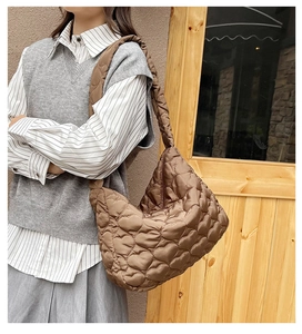 Detail of a brown heart-quilted tote bag worn by a model in a casual autumn outfit