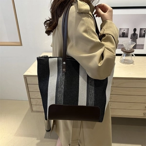 Detail of striped canvas tote bag with brown leather base and shoulder straps on a model