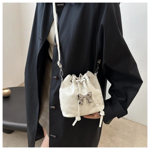 Detail of white pleated bucket bag with silver metal bow and drawstring on model