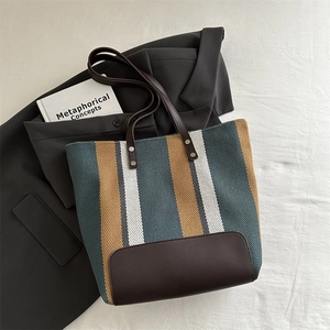 Detail of striped canvas tote with brown leather base and metallic rivets on gray blazer