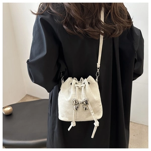 Detail of white drawstring bucket bag featuring a silver metal bow and textured faux leather
