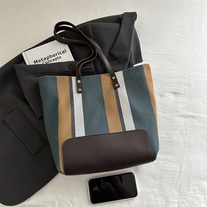Detailed close-up of a striped canvas tote bag with brown leather handles and base