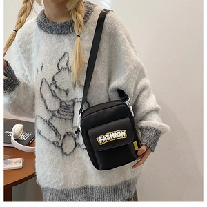 Detail of black nylon crossbody bag with fashion patch and adjustable strap on a model