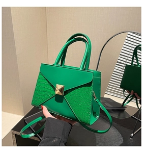 Detail of green faux leather bag with crocodile pattern and golden pyramid stud closure