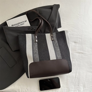 Detail of striped woven tote bag with brown leather handles and stitching accents