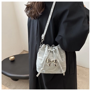 Detail view of light grey pleated drawstring bucket bag with silver metal bow accent