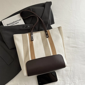 Detail of the striped canvas tote bag showing reinforced leather base and silver rivets
