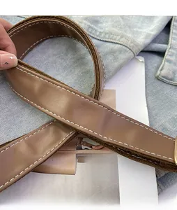 Détail d'une bandoulière en cuir marron avec surpiqûres blanches et boucle dorée