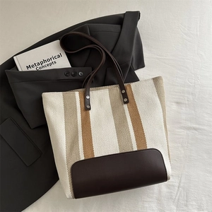 Close-up of striped canvas tote bag with brown leather handles and rivet details