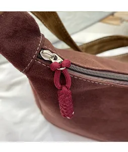 Détail d'une fermeture éclair en métal argenté avec cordon rouge sur un sac en daim marron