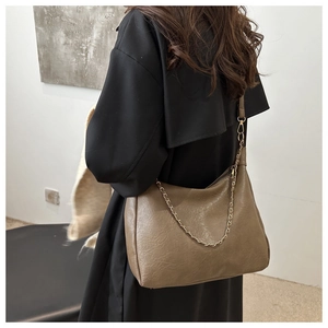 Détail du sac cabas en cuir vert olive avec chaîne dorée sur l'épaule du mannequin