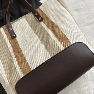 Detail of striped canvas tote showing woven texture, leather trim and metal rivets