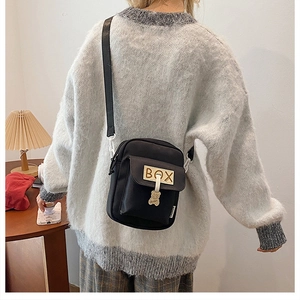 Close-up of black canvas crossbody bag with BOX embroidery and cute bear charm detail