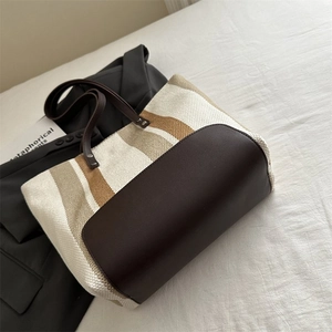 Detailed top view of striped canvas tote bag with brown leather trim on white textured bedding