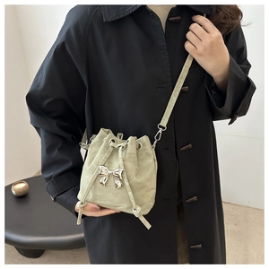 Detail of sage green pleated bucket bag with silver bow charm on a black coat