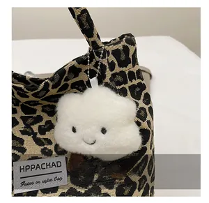Detail shot of leopard print tote bag with white plush cloud charm and stitched brand label