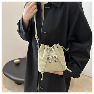 Close-up of a light green drawstring bucket bag featuring a silver metal bow accent