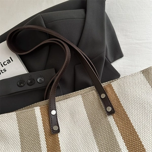 Close-up of woven striped tote bag with dark brown leather handle and silver rivet details