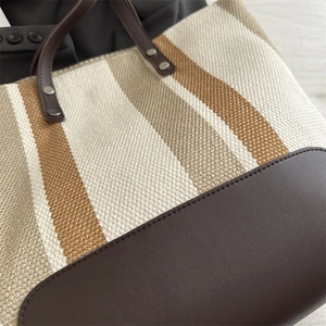 Close-up detail of striped canvas tote bag showing leather stitching and metal rivets