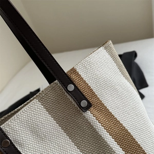 Detail of striped canvas tote showing leather handle, silver rivets and stitching