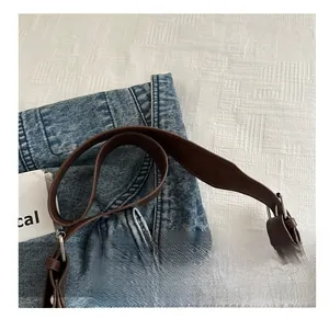 Close-up of brown leather shoulder bag strap with silver metal buckle on denim fabric