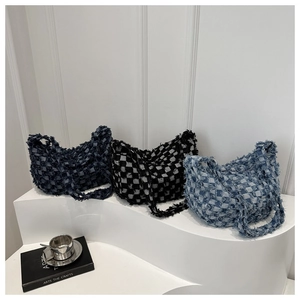 Three denim checkerboard shoulder bags with fringe edges on white display stand