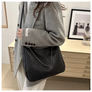 Détail du sac cabas en cuir noir avec chaîne dorée porté sur un blazer gris