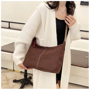 Détail du sac cabas vintage en daim marron avec surpiqûres et breloque tissée élégante