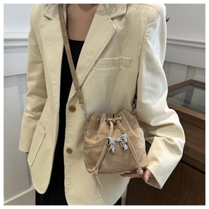 Detail of beige pleated drawstring bucket bag with a silver metal bow accent