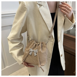 Detail of beige pleated drawstring bucket bag with silver bow accent and adjustable strap