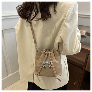 Detail view of beige pleated bucket bag with silver bow buckle and drawstring closure