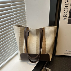 Close-up of striped canvas tote bag with brown leather base and dual shoulder straps