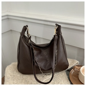 Détail du sac cabas marron foncé en cuir avec chaîne sur un fond en tricot beige