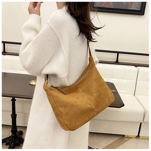 Détail d'un sac hobo en daim marron avec forme demi-lune et pompon tressé sur la fermeture