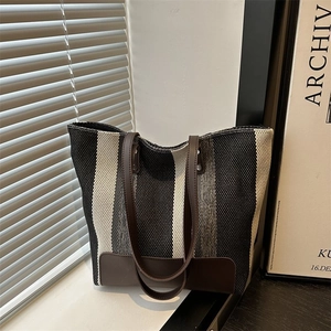 Detailed view of striped canvas tote bag with brown leather handles and woven texture