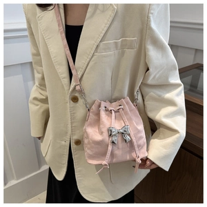 Close-up of pink pleated bucket bag with silver bow accent on model in beige blazer