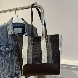 Close-up of a striped canvas tote bag with dark brown leather straps and rivet accents