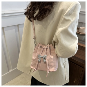 Detailed side view of light pink pleated bucket bag with silver bow on cream blazer
