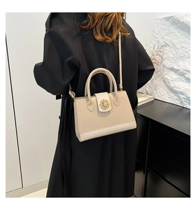 Sac fourre-tout beige avec texture crocodile et boucle fleur dorée sur trench-coat noir
