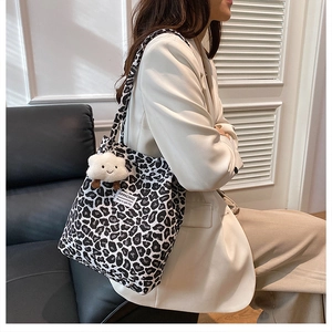 Macro detail of leopard print canvas tote bag with a white plush cloud charm and strap