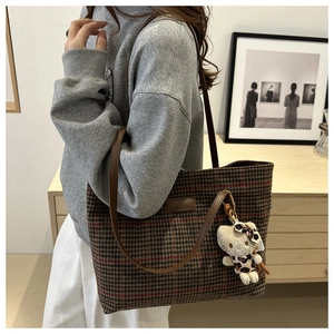Detailansicht der braunen Canvas-Tasche mit Karomuster, Lederriemen und Katzenanhänger
