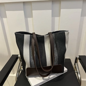 Detail of striped canvas tote bag with brown leather handles on a leather chair
