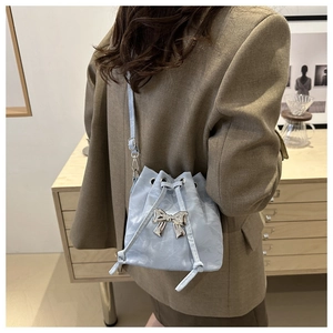 Ice blue drawstring bucket bag featuring a metallic silver bow on a pleated surface