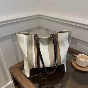 Close-up of striped canvas tote bag with brown leather handles and textured fabric