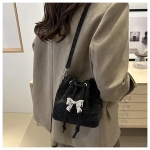 Detail view of black pleated velvet bucket bag with a silver metallic bow and drawstring
